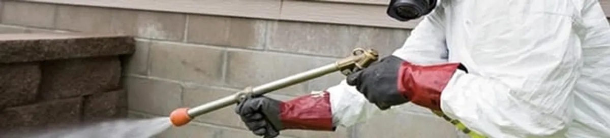 Pest control technician applying exterior insect treatment along a home foundation in Savannah, GA