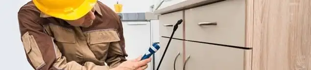 Roach exterminator applying treatment under kitchen cabinets in Savannah, GA
