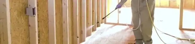 Termite treatment technician applying spray along framing and unfinished walls in Savannah, GA